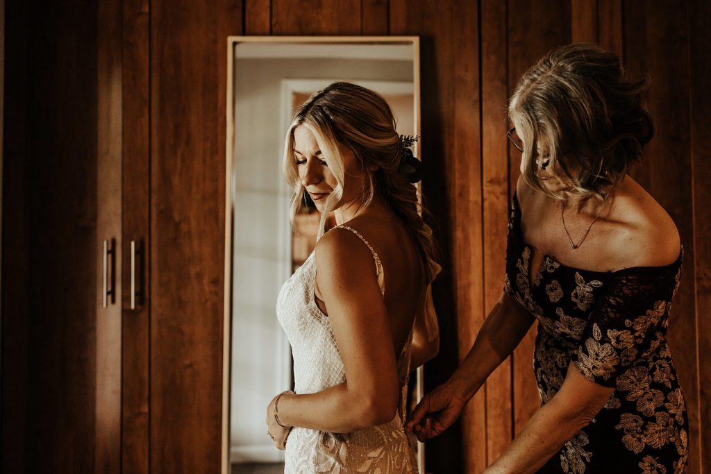 Mother helping daughter into bridal gown by Jennifer's Bridal