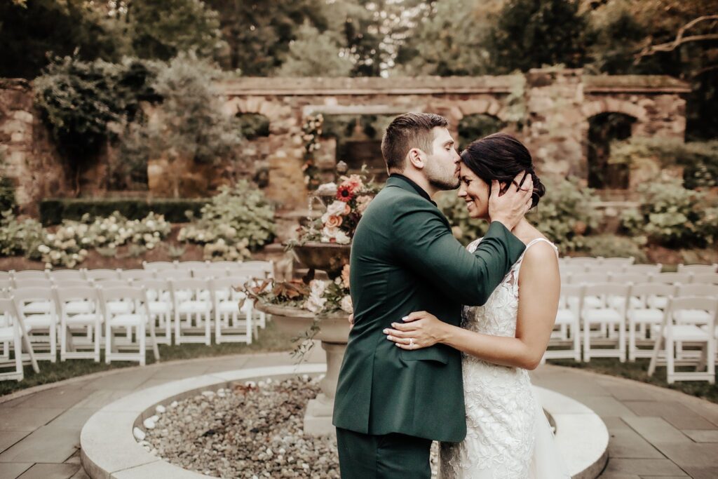 Post Wedding Forehead Kiss at outdoor venue in green suit and lace dress