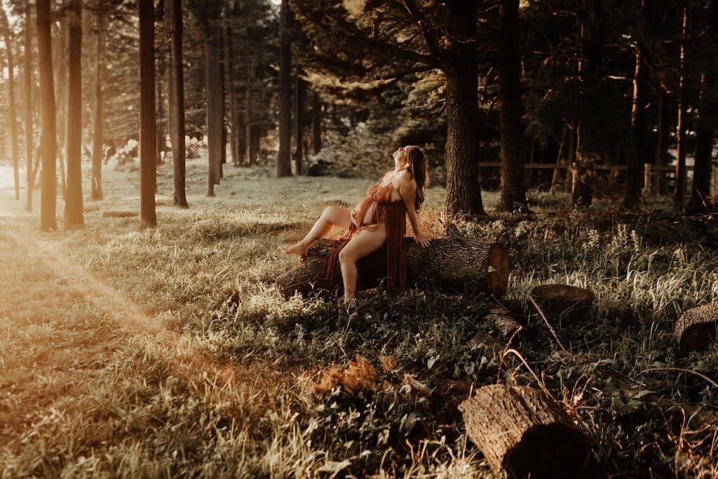 Pregnant woman holding her belly and sitting on a log in the woods