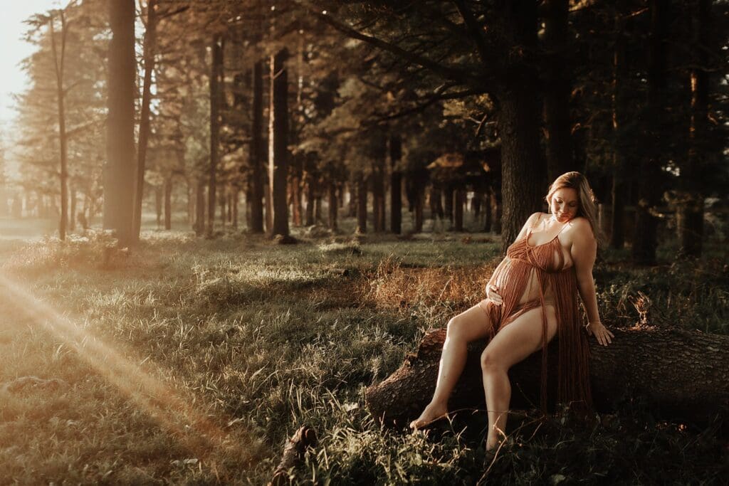 Pregnant woman holding her belly while sitting on a log in the woods